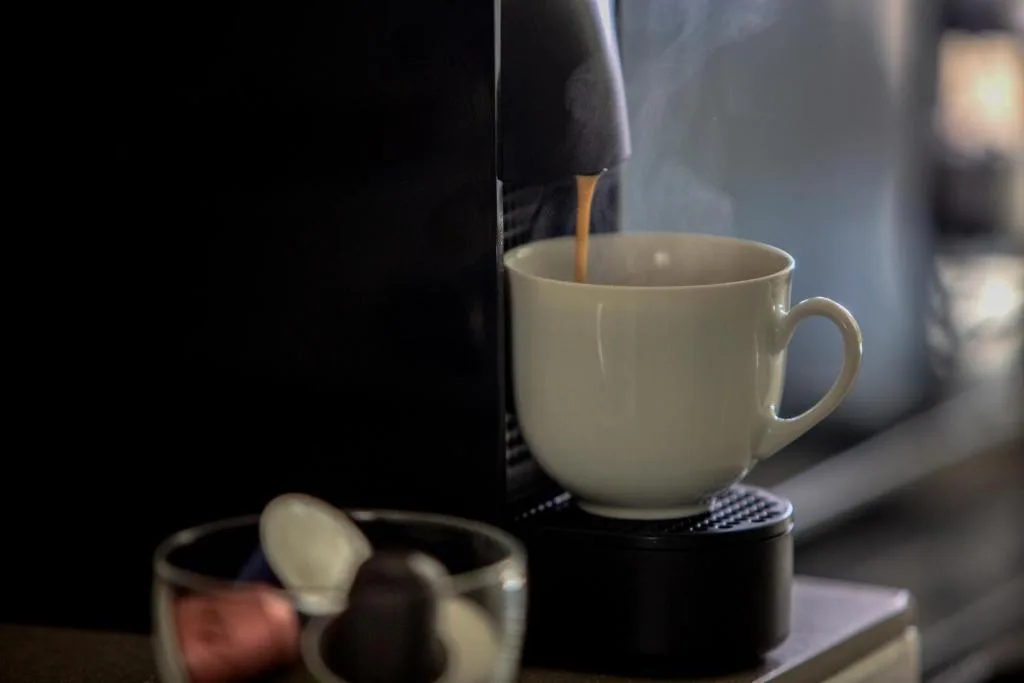 Coffee being poured into white ceramic mug near modern coffee machine