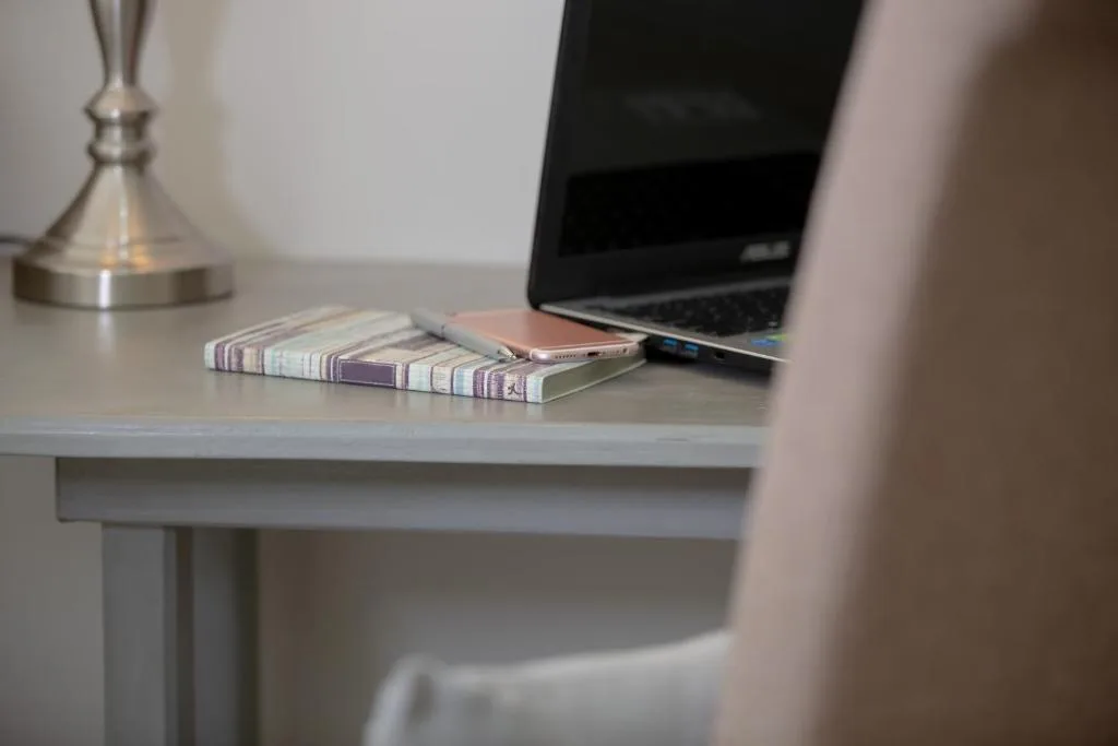 Workspace desk with laptop, notebook, phone and desk lamp