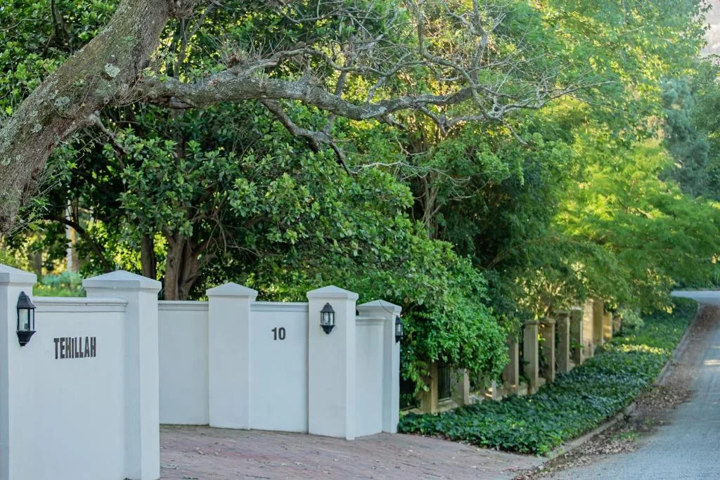 White entrance gate and property signage surrounded by lush green vegetation