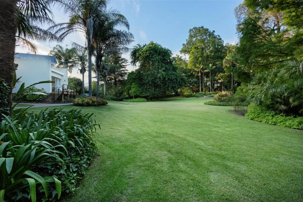 White cottage with manicured lawn and lush tropical garden surroundings