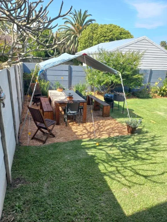 Shaded outdoor dining area with table, chairs, and lush garden surroundings