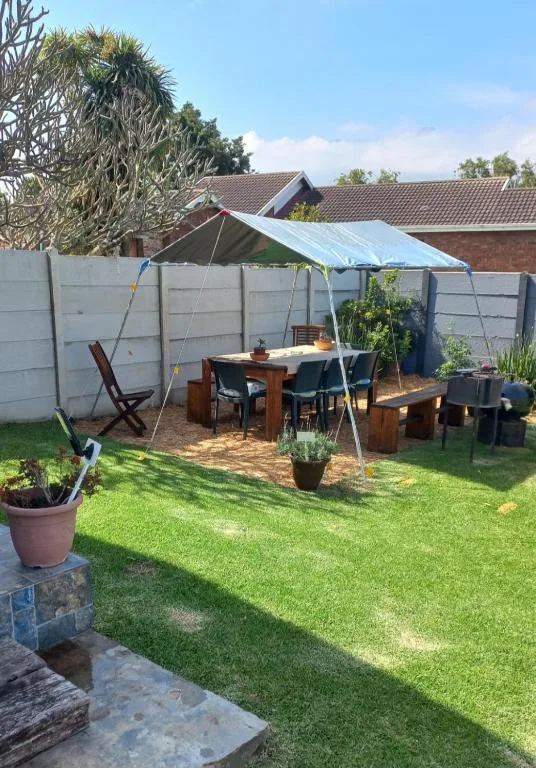 Shaded outdoor dining area with table, benches, and potted plants in garden
