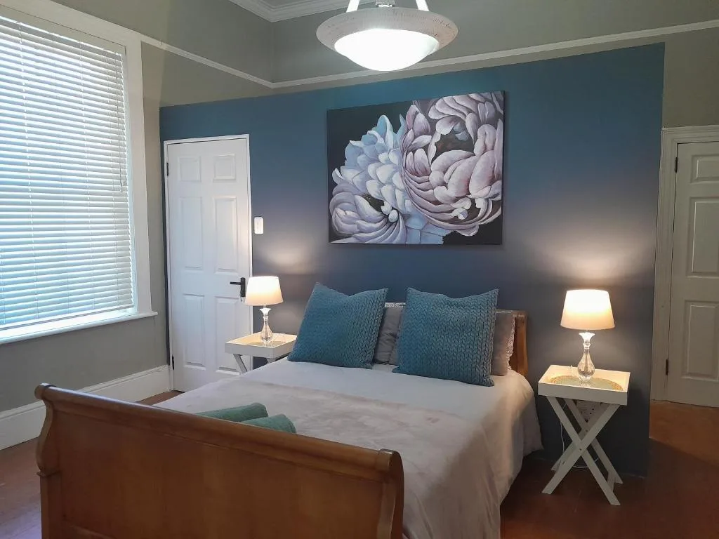 Spacious bedroom with wooden bed, teal accent wall, floral artwork, and bedside lamps