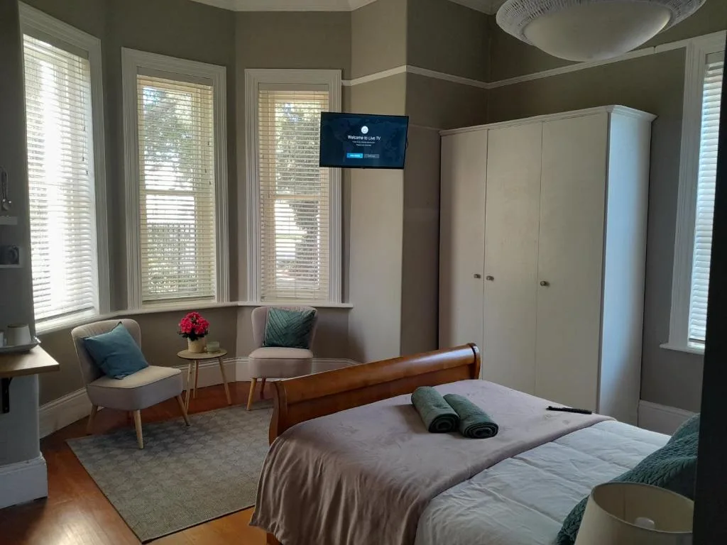 Spacious bedroom with wooden bed, white wardrobes, and comfortable seating area