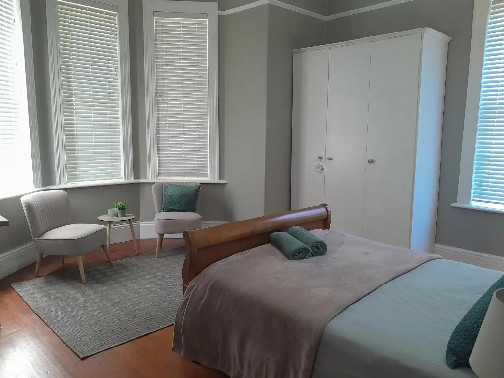 Spacious bedroom with bed, seating area, wardrobe, and bright windows