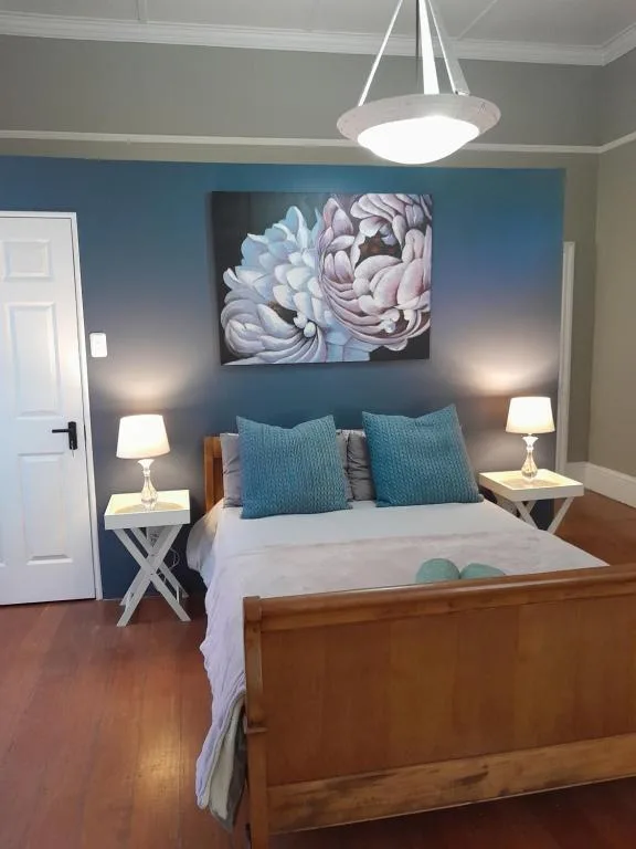 Bedroom with wooden bed, blue accent wall, and floral artwork above