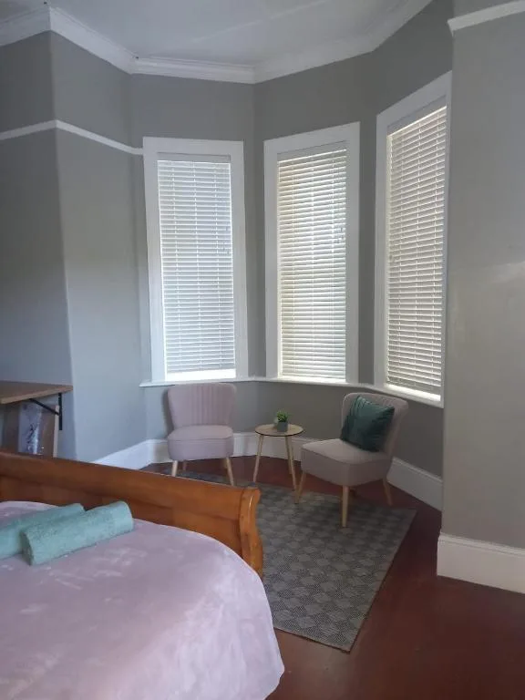 Spacious bedroom with wooden bed, bay window seating area with chairs