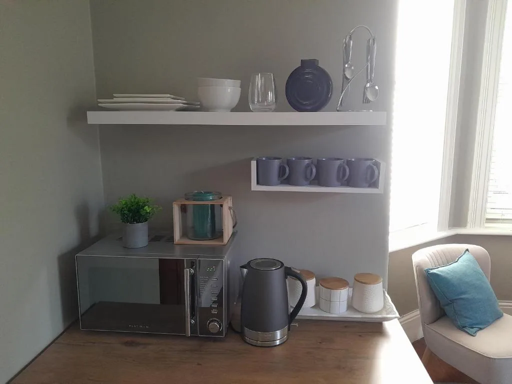 Modern kitchen corner with shelving, microwave, kettle, and dining setup