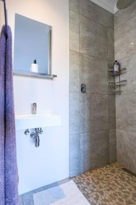 Modern bathroom with gray tile shower, white vanity, and purple towel