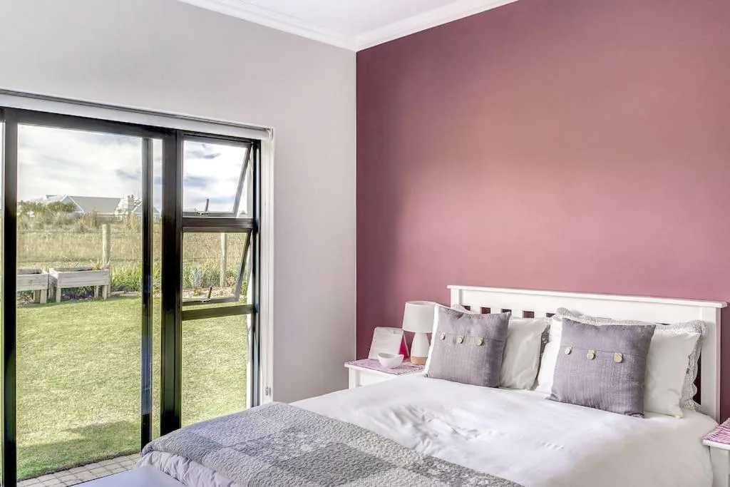 Master bedroom with mauve accent wall and garden views through glass doors
