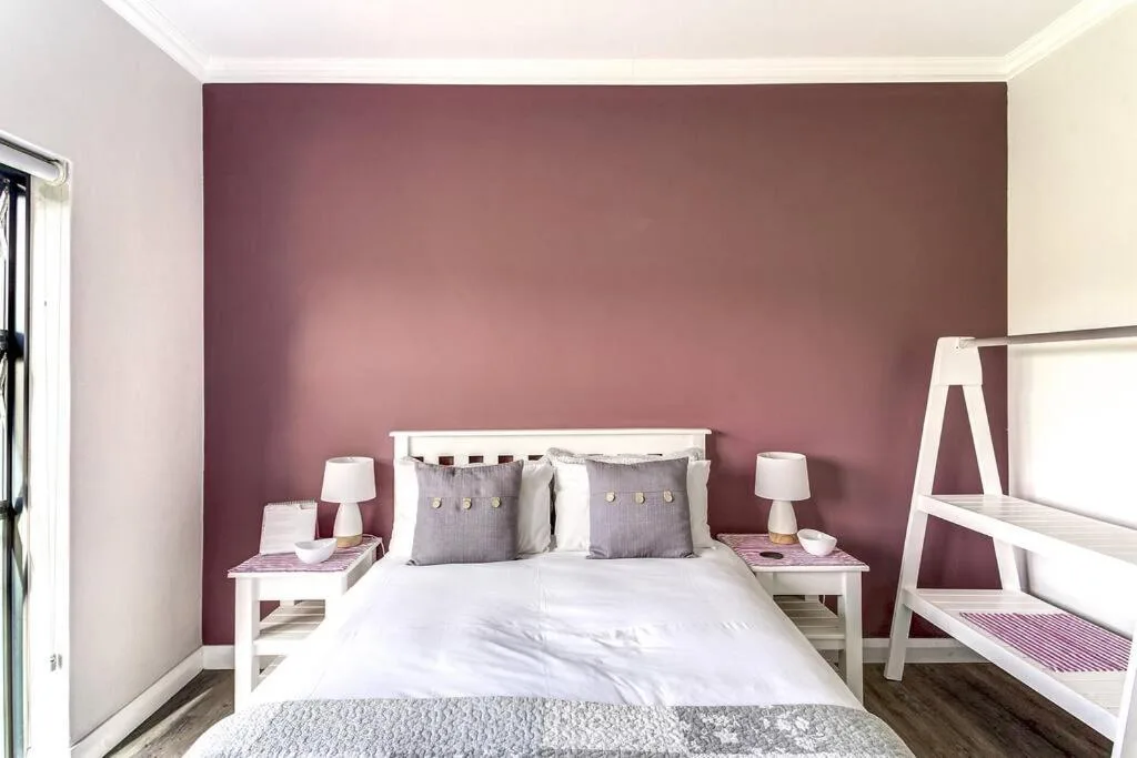 Modern bedroom with burgundy accent wall, white bed, grey pillows, matching nightstands
