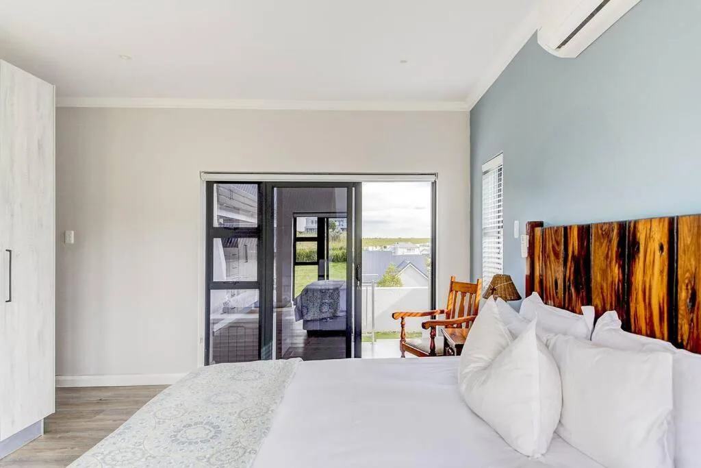 Spacious bedroom with white bedding, wooden headboard, and sliding doors to deck
