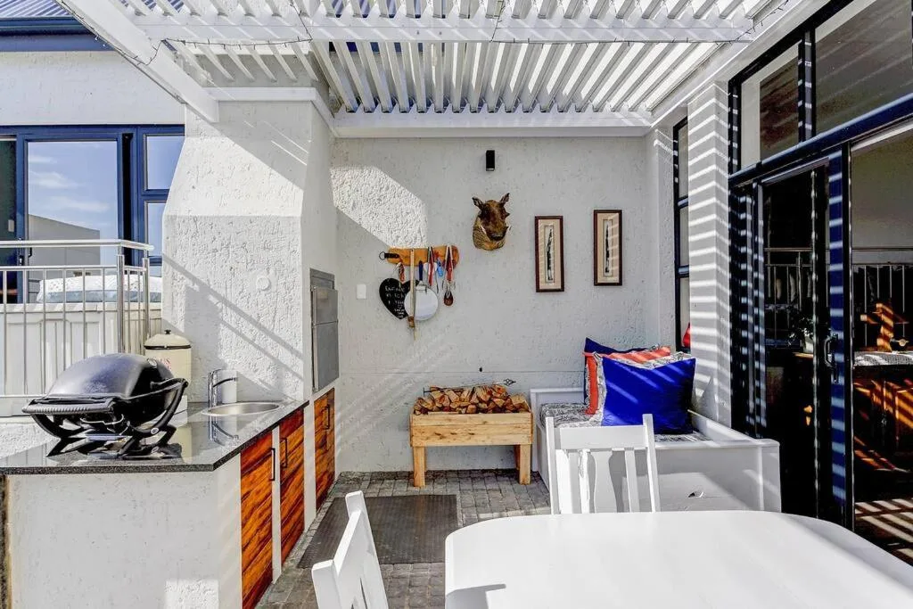 Covered outdoor patio with braai area, seating, and white pergola roof