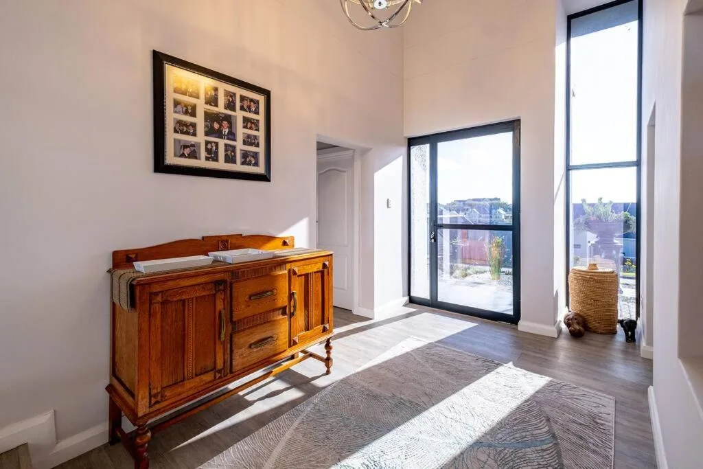 Bright hallway with wooden dresser, framed photos, and garden views through glass doors