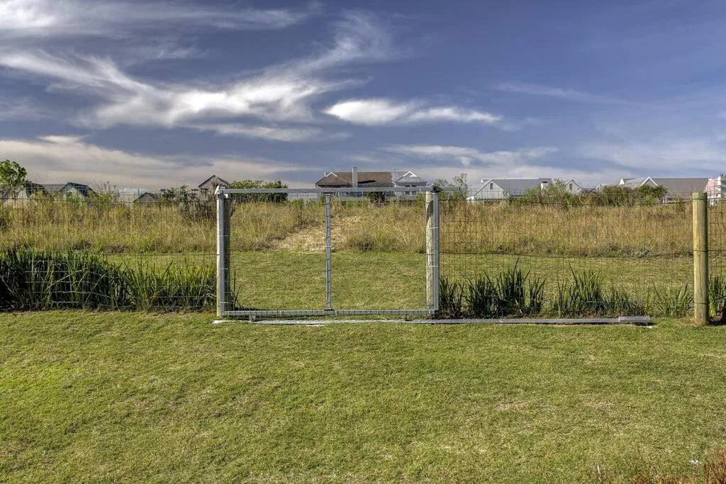 Rural property with spacious grounds, fencing, and distant houses under cloudy sky