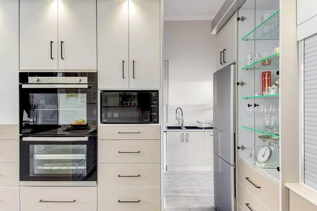Modern white kitchen with built-in oven, microwave, refrigerator and green glass shelving