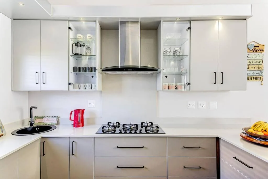 Modern white kitchen with gas cooktop, range hood, and open shelving