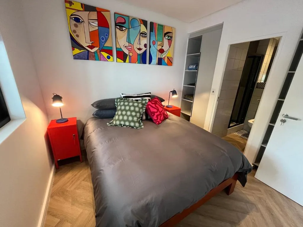 Modern bedroom with colorful abstract face artwork and bright red accent furniture