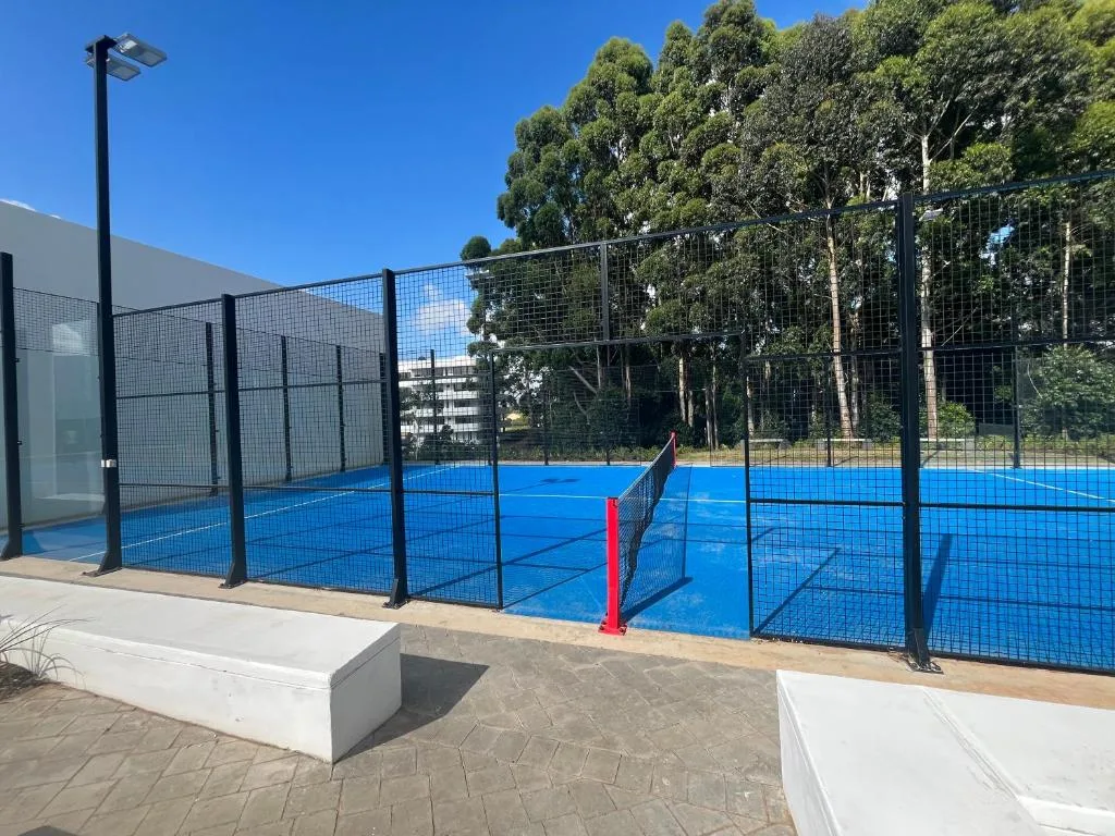 Blue paddle tennis court with black netting and red net divider