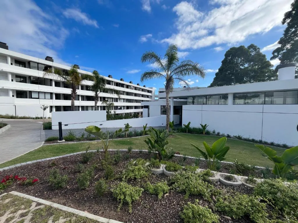 Modern white apartment building with manicured gardens and palm trees