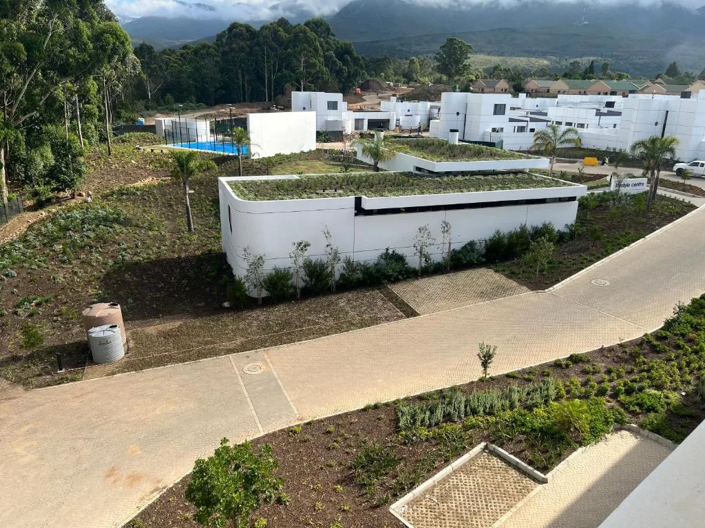 Modern white property with green roof and paved driveway, mountain backdrop visible