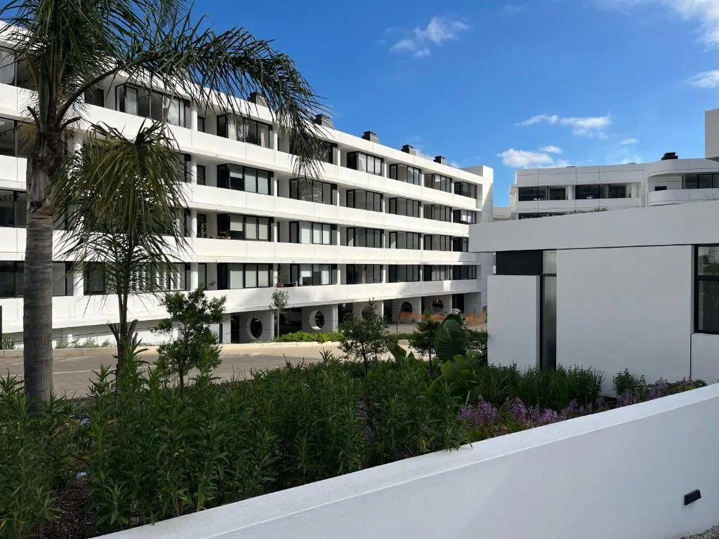 Modern white apartment building with palm trees and flowering garden beds