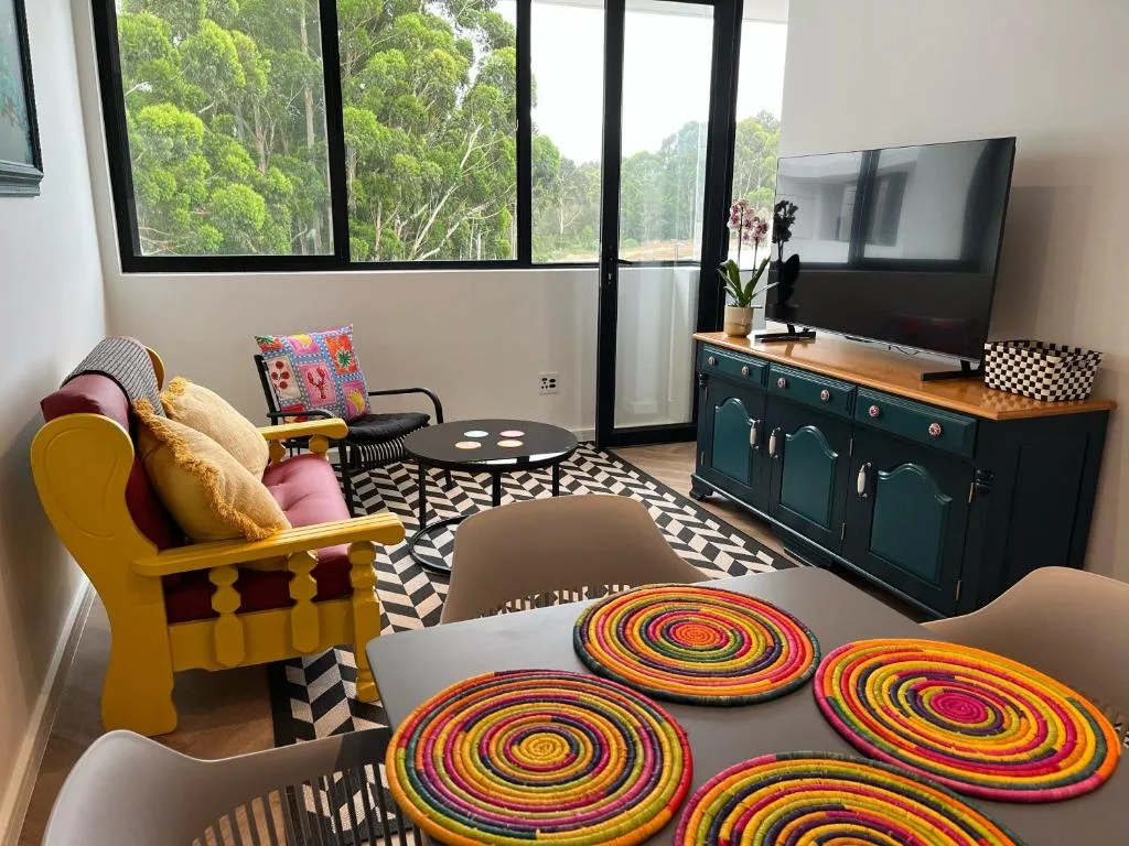 Modern lounge with yellow armchair, TV, forest views through large windows