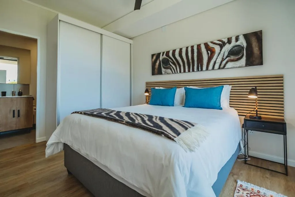 Modern bedroom with queen bed, blue pillows, zebra artwork, and wooden headboard