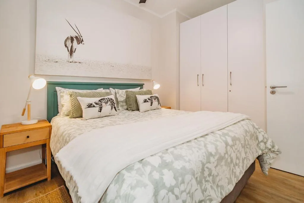 Modern bedroom with green headboard, white bedding, wildlife artwork above bed