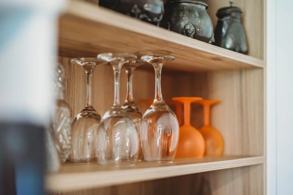 Wooden shelf displaying wine glasses and decorative orange vases