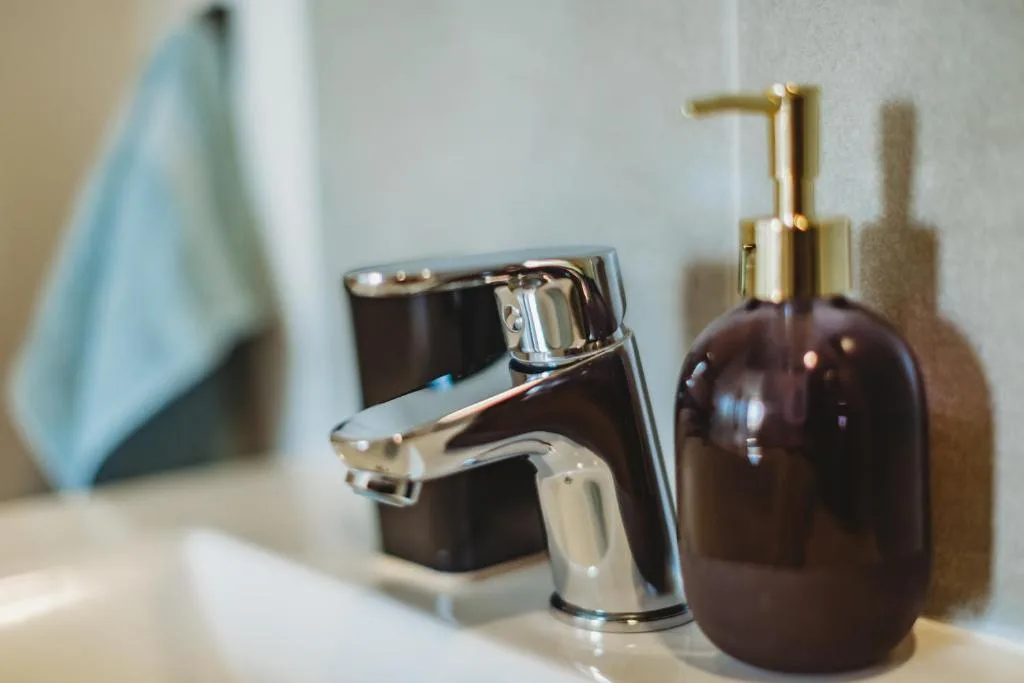Modern chrome bathroom faucet with dark soap dispenser and hand towel