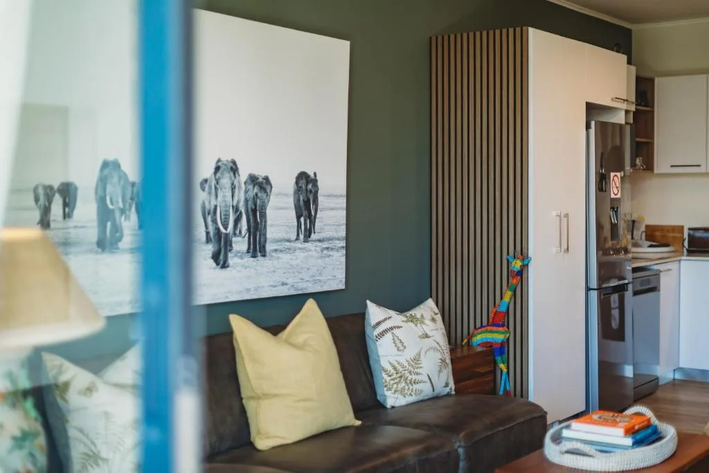 Modern lounge with dark sofa, elephant artwork, and open-plan kitchen view