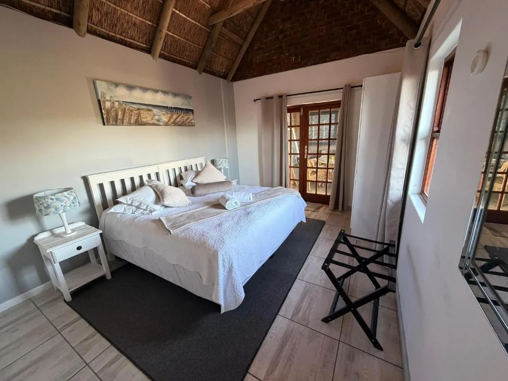 Bright bedroom with white bed, thatched ceiling, and wooden doors opening to garden