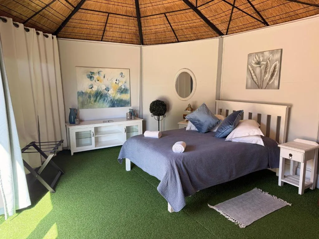 Bright bedroom with double bed, white furniture, thatched ceiling, and artwork