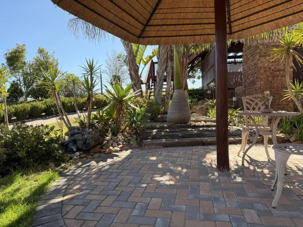 Thatched pergola with paving, tropical plants, and white garden furniture