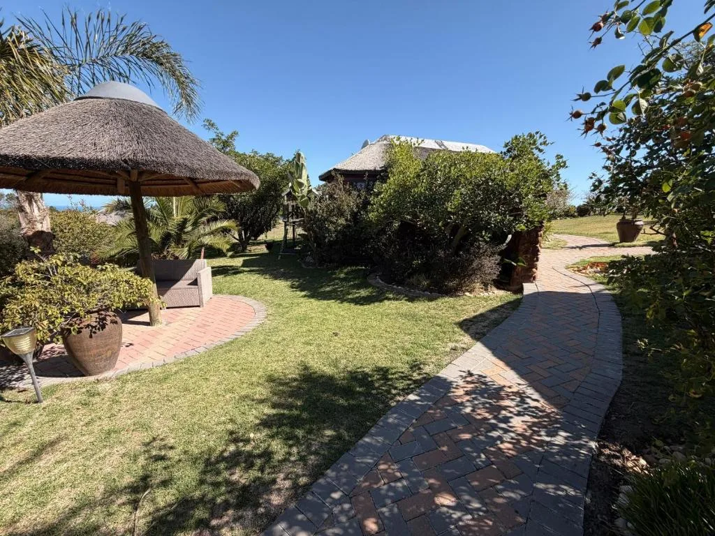 Thatched-roof villa with manicured gardens and brick pathways under blue sky