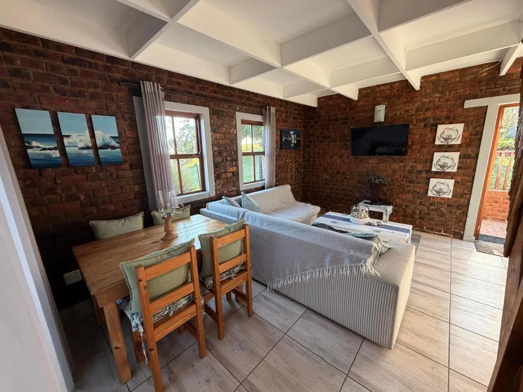 Open-plan lounge with sofa, dining table, brick walls, and TV