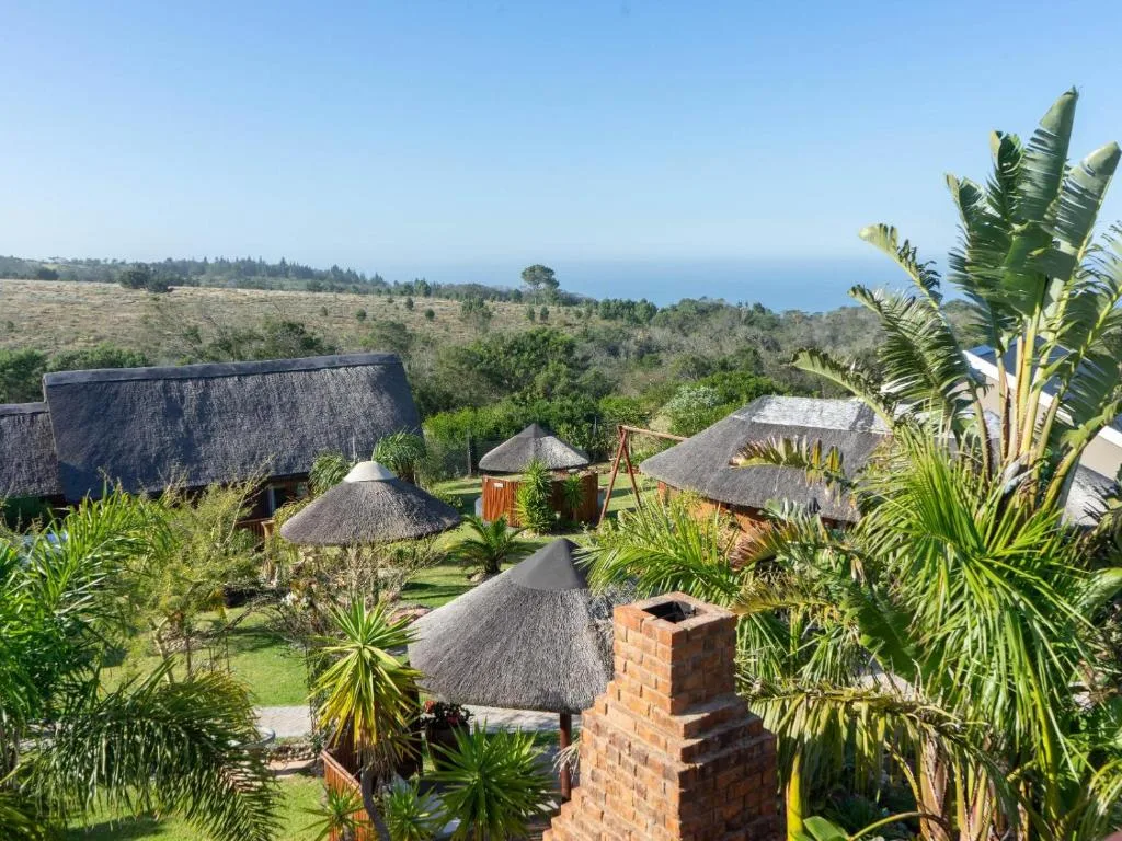 Ocean and forested landscape view from property with thatched-roof buildings
