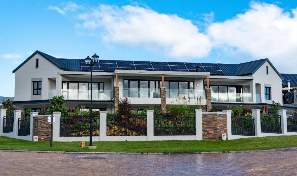 Modern white house with dark roof and solar panels, manicured garden