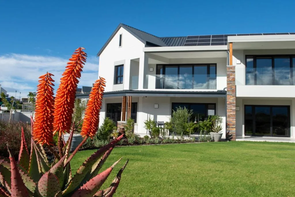 Modern white house with solar panels and manicured garden landscape