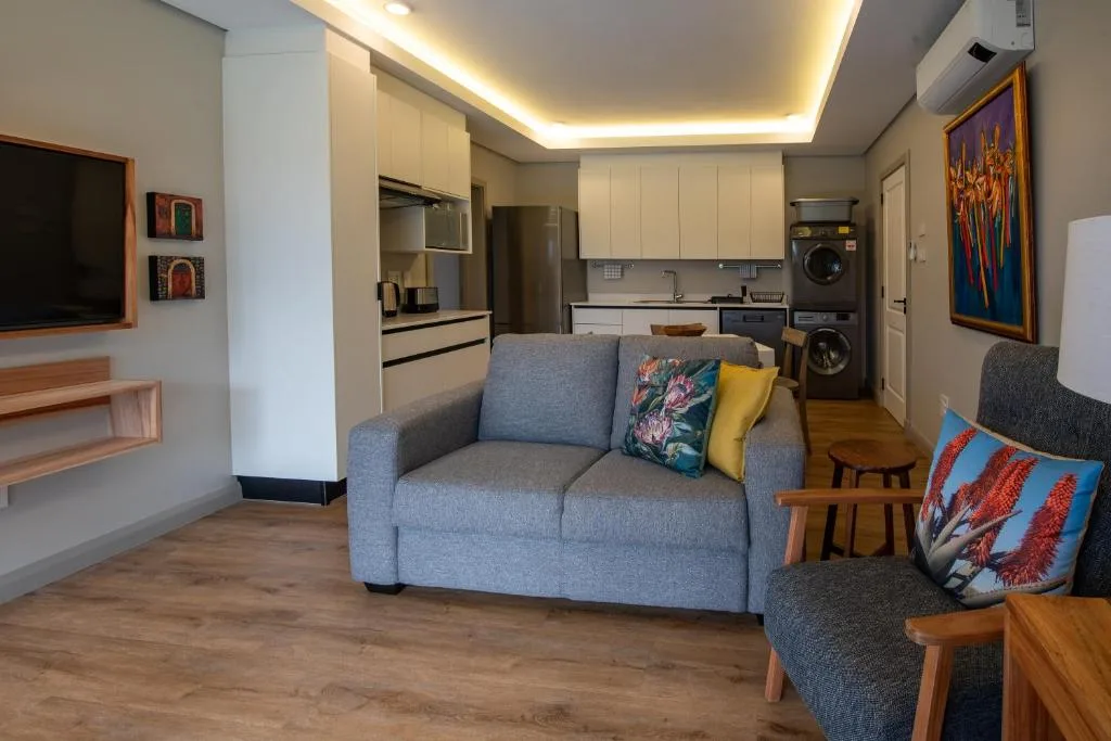 Modern living room with gray sofa, colorful cushions, and open-plan kitchen