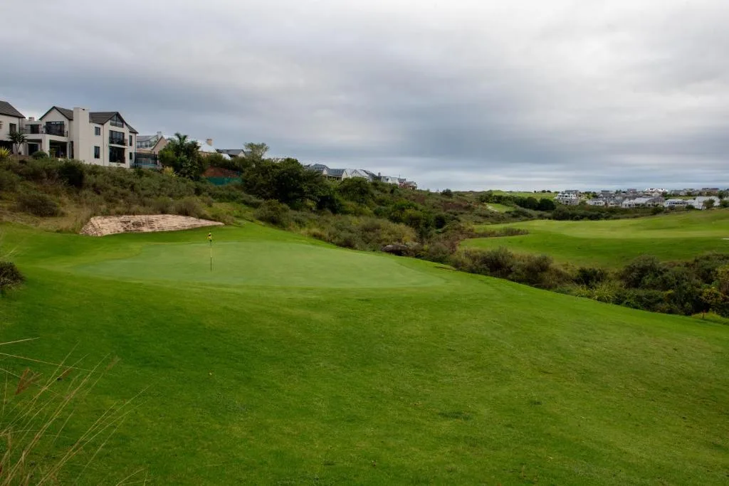 Expansive green golf course with modern houses and rolling landscape beyond