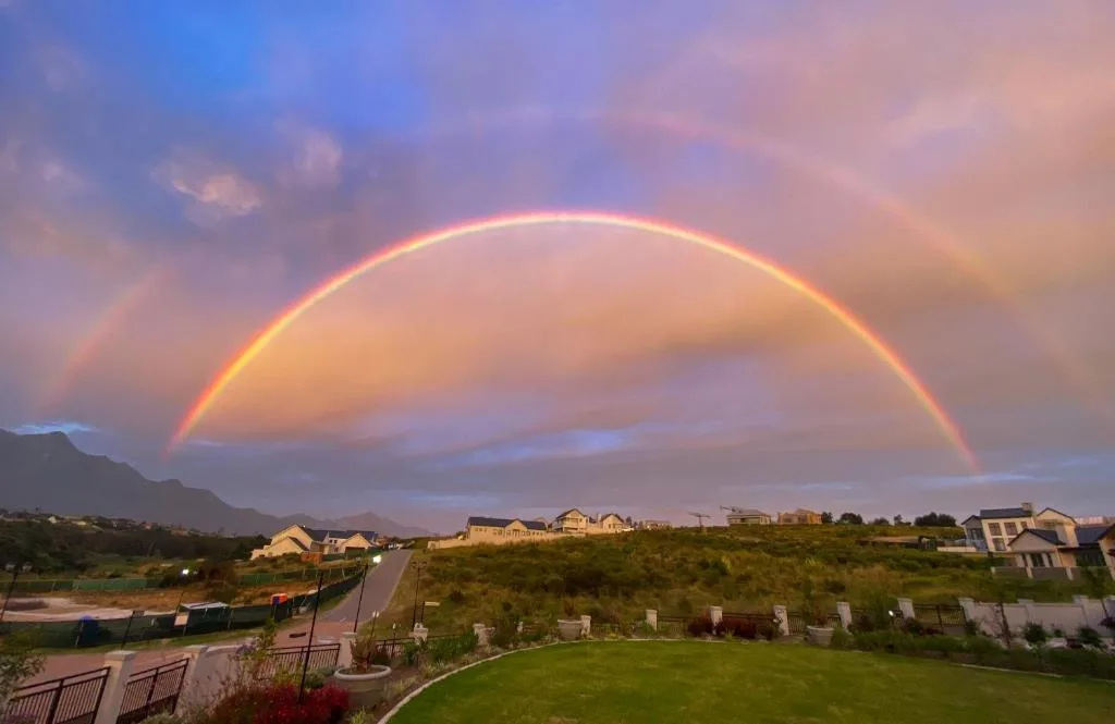 Dramatic rainbow arching over mountain landscape and residential estate at dusk