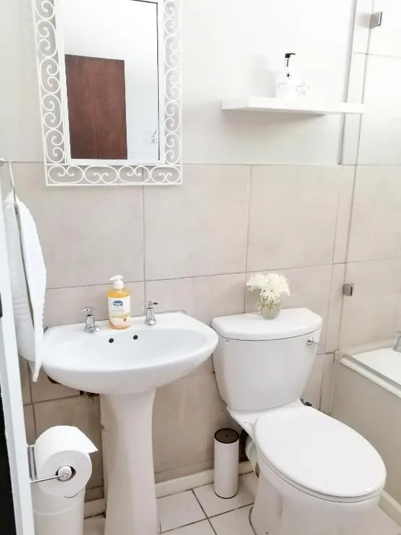 Clean bathroom with pedestal sink, toilet, mirror, and tiled walls