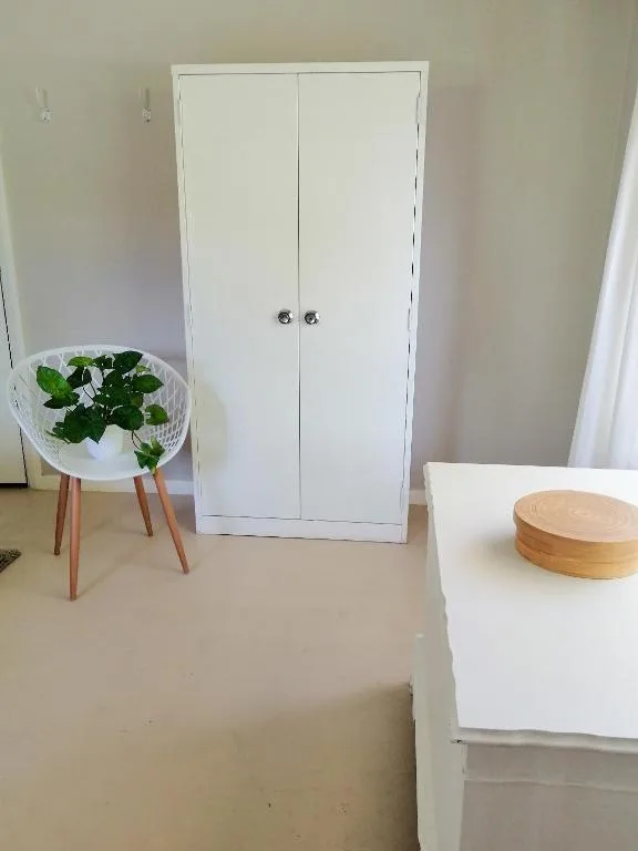 White wardrobe cabinet with potted plant and wooden accessories in modern bedroom