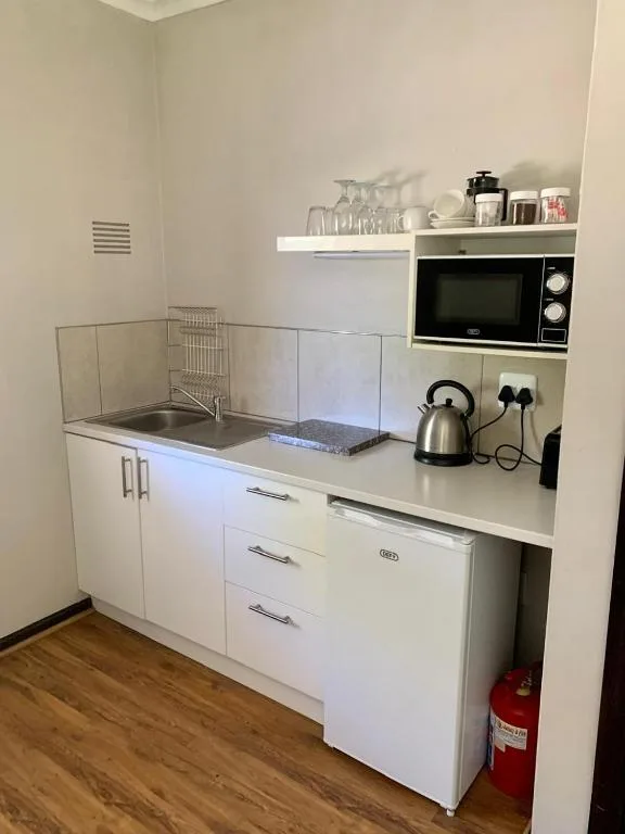Compact white kitchen with microwave, kettle, and open shelving above sink