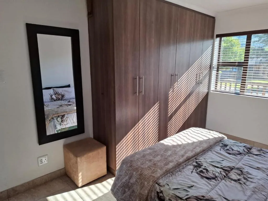 Modern bedroom with bed, dark wood wardrobe, and sunlit windows