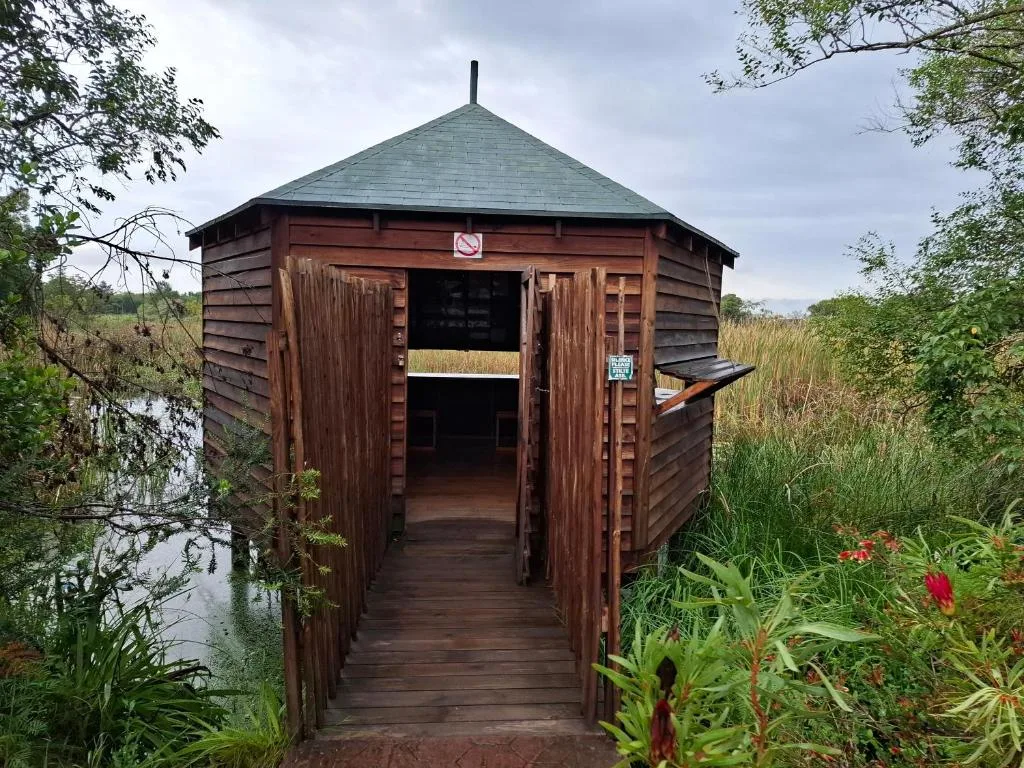 Wooden octagonal cabin with boardwalk entrance surrounded by lush garden vegetation