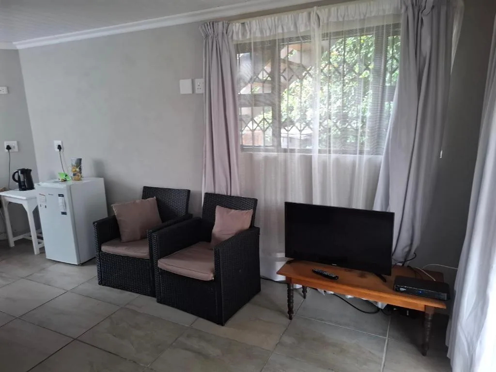 Living room with black rattan seating, TV, and large windows overlooking garden