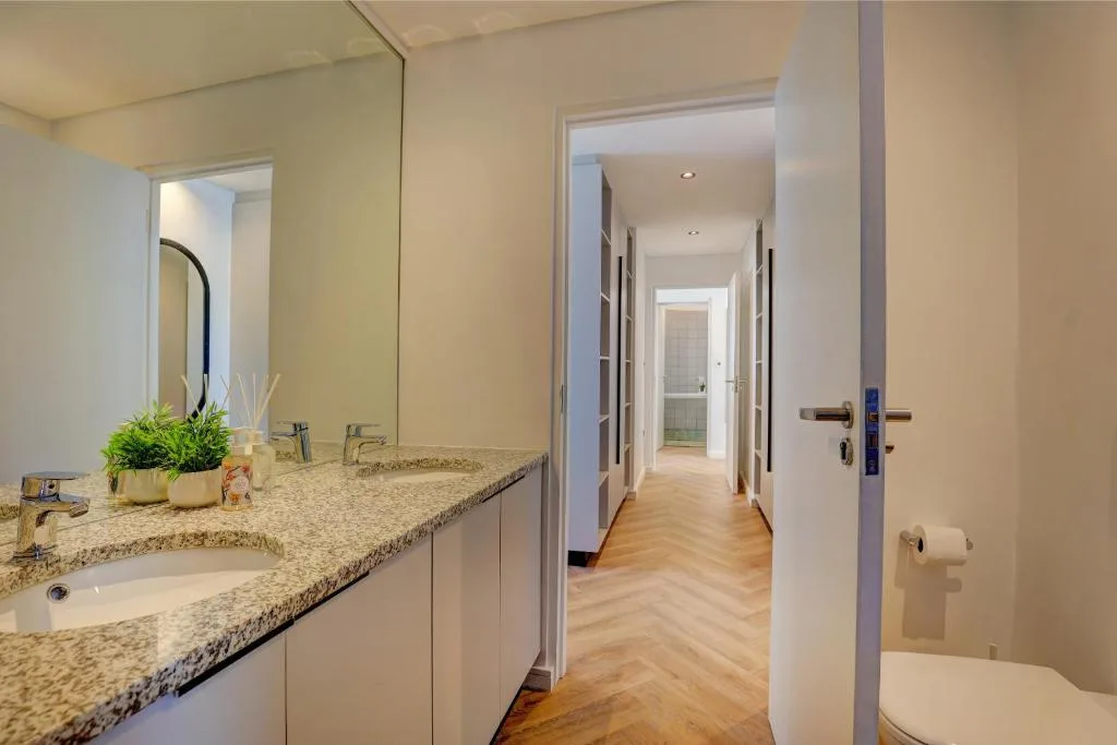 Modern bathroom with granite vanity, large mirror, and herringbone wood flooring